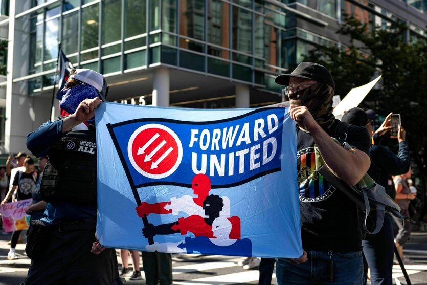 Zwei vermummte Männer halten ein Transparent hoch mit der Losung: Forward United
