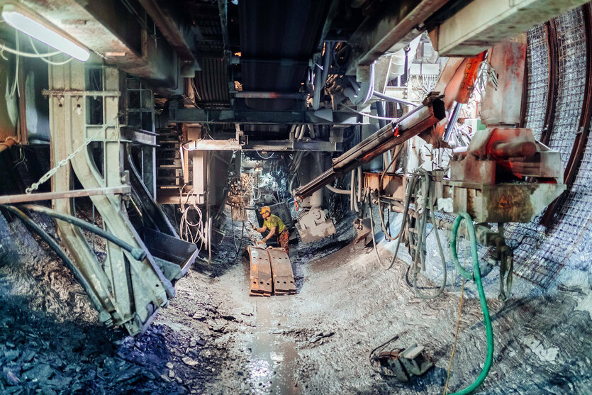 Eine Person mit Arbeitskleidung und Schutzhelm arbeitet beim Bau eines Tunnels unter der Erde an der Tunnelbohrmaschine.