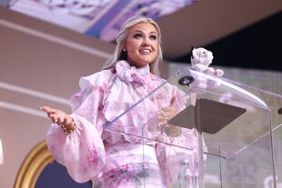 Erika Kirk an einem gläsernen Stehpult. Sie ist ganz in rosa gekleidet