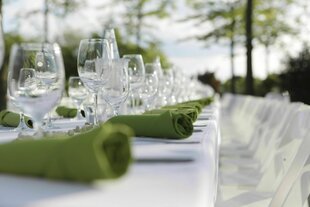 Ein festlich gedeckter Tisch im Freien, mit weißer Tischdecke und grünen Servietten