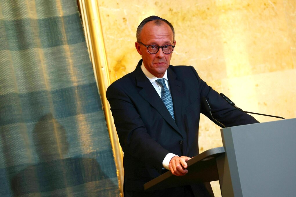 Friedrich Merz steht mit Kippa auf dem Kopf am Rednerpult und wirkt sehr bewegt