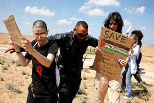 Ein israelischer Polizist verdrängt zwei protestierende Frauen, die Protestschilder in der Hand halten