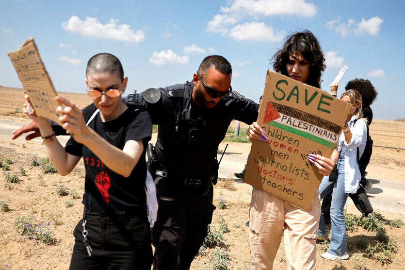 Ein israelischer Polizist verdrängt zwei protestierende Frauen, die Protestschilder in der Hand halten