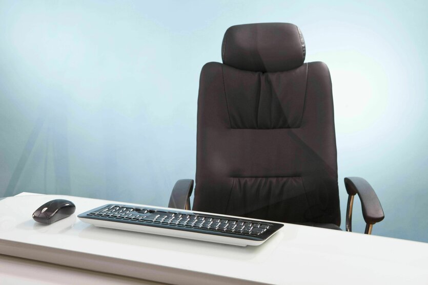 Ein leerer Bürostuhl aus Leder steht vor einem Tisch, auf dem eine Maus mit Tastatur liegt