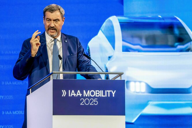 Markus Söder am Rednerpult auf dem IAA Mobility 2025 steht, und ein Auto als PRojektion im Hintergrund