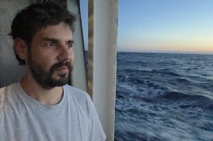 Ein junger Mann mit Bart und strubeligen Haaren schaut von einem Schiff aus aufs Meer
