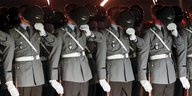 Vier Soldaten halten sich die Helme vors Gesicht.