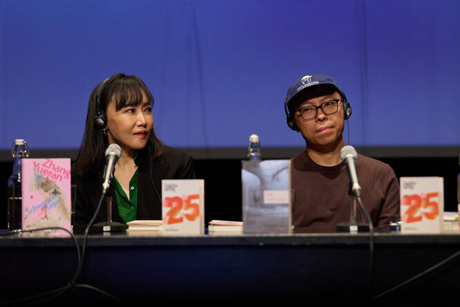Zwei Menschen sitzen mit Kopfhörern auf der Bühne