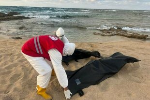 Zwei Menschen sind am Strand und schließen Leichensäcke