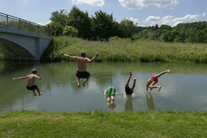 Mehrere Jugendliche springen in einen Fluss.