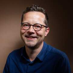 Zu sehen ist der Autor Jörn Kabisch, er trägt ein blaues Hemd und eine Brille.