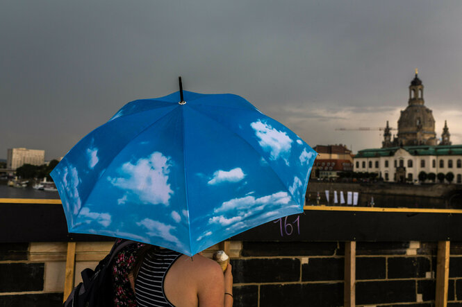 Frau läuft mit einem Regenschirm auf dem blauer Himmel und Wolken zu sehen sind