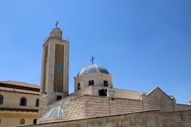 Außenansicht einer Kirche aus hellem Stein, auf deren Turm und Kuppeö das Kreuz angebracht ist