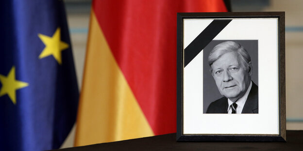 Ein Portrait steht vor einer Deutschland und einer Europafahne