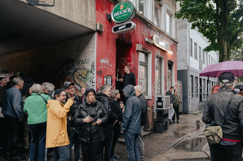 Menschen stehen vor einem Haus mit roter Fassade, Graffiti und Bierwerbung.