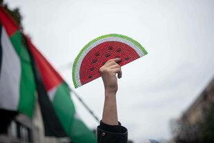 Demonstrierende hält Wassermelonen-Schild hoch, im Hintergrund Palästinaflaggen