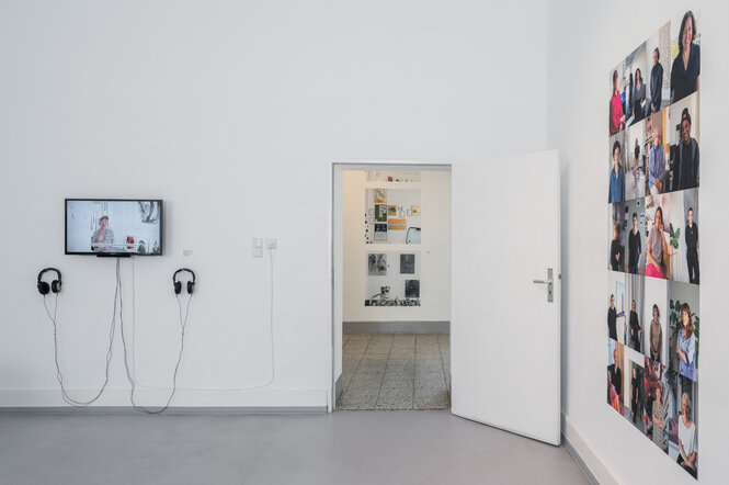 Im Ausstellungsraum hängt eine Videoarbeit an der Wand, daneben hängt eine Ansammlung von Fotoproträts, die Künstlerinnen zeigen und randlos nebeneinander gehängt sind.