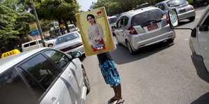 Ein Mann steht zwischen Autos auf der Straße in Birma. Er hält ein Plakat mit Aung San Suu Kyi, es verdeckt seinen Rücken und das Gesicht