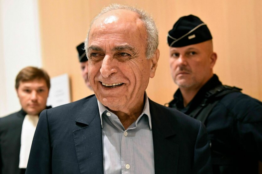 Ziad Takieddine lächelt in die Kamera, hinter ihm stehen zwei Polizisten