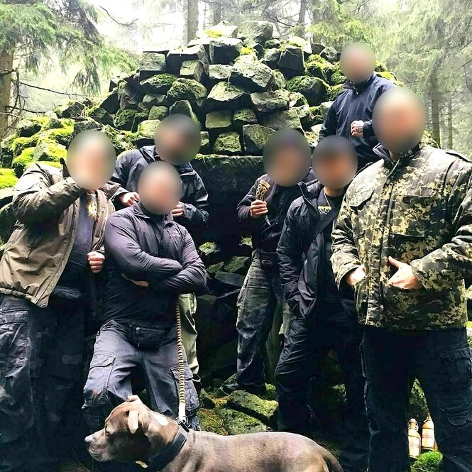 Gruppenfoto von mittelalten Männern im Wald, viele im Camouflage-Outfit und gepixelten Gesichtern