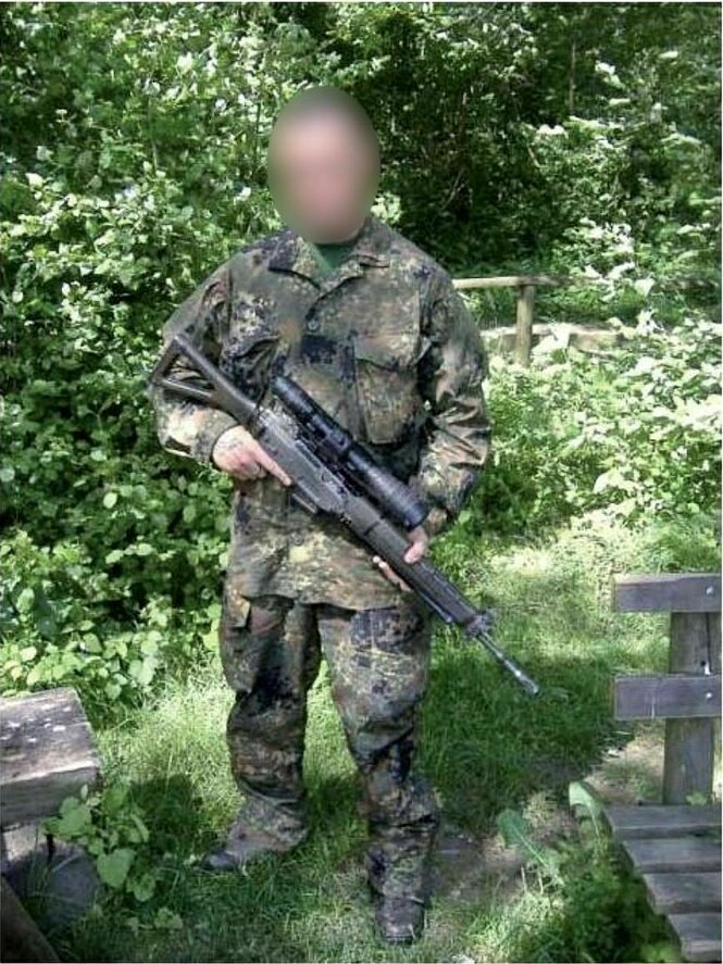 Ein mit einem Maschinengewehr bewaffneter Mann steht im Tarnanzug im Grünen