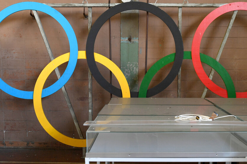Das Bild zeigt die Olympischen Ringe hinter anderen Gegenständen.