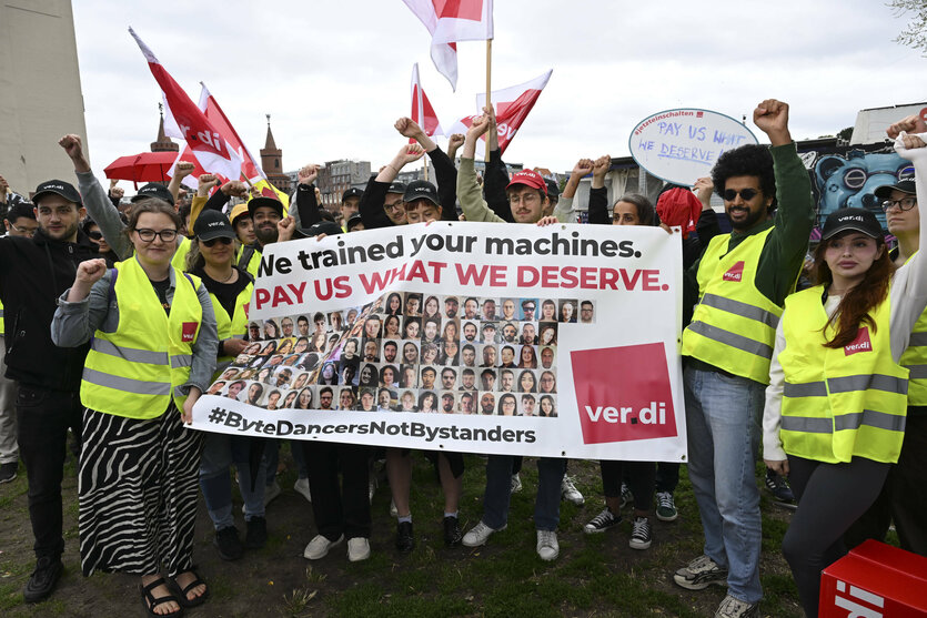 Tiktok Mitarbeiter in gelben Warnwesten protestieren gegen ihre Kündigung und halten ein Plakat hoch mit "Pay us what we deserve"