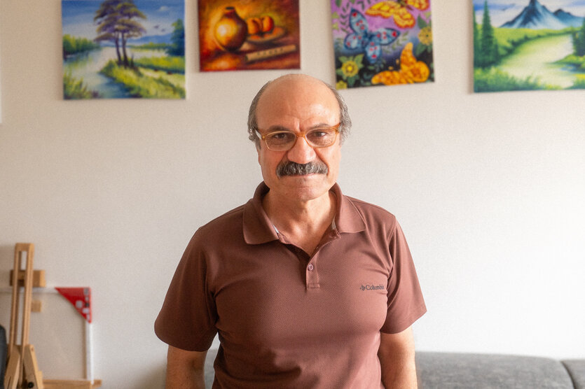 Osman, Schnurrbart, braunes Poloshirt, im Hintergrund seine Malerei