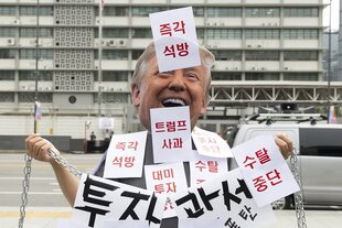 Jemand trägt eine Maske mit dem gesicht Donald TRumps und viele Zettel mit Koreanischen Buchstaben