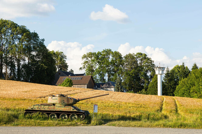 Ein Wachturm und eine alter Panzer stehen in der Landschaft.