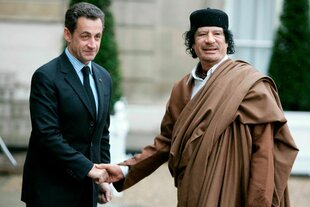 Nicolas Sarkozy begrüßt Moammar Gadhafi, der in ein braunes Gewand gehüllt ist