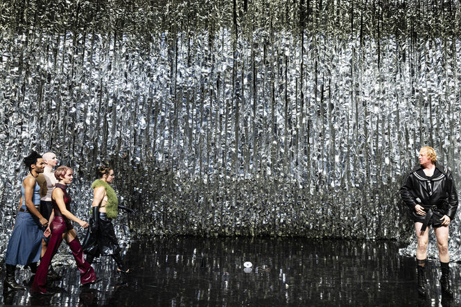 Vier Schauspieler:Innen von links rennen auf einen Schauspieler mit nassem Matrosenanzug am rechten Rand zu. Der Hintergrund besteht aus Lametta