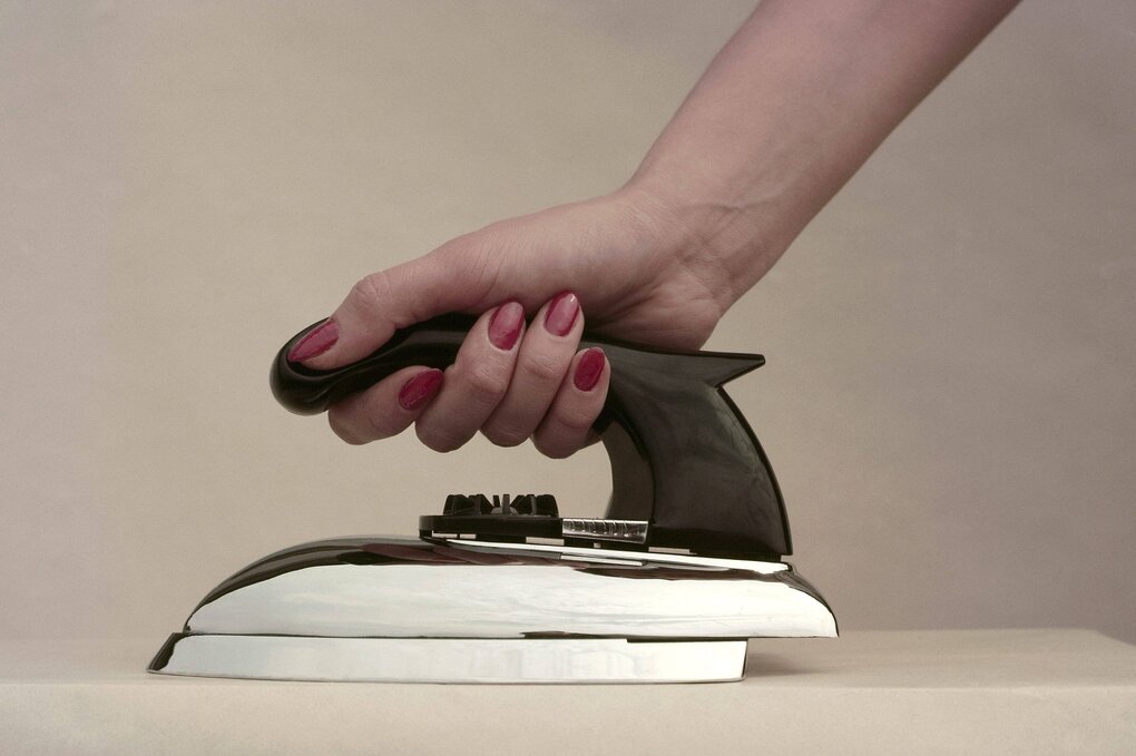 Eine Frauenhand mit rotlackierten Fingernägeln hält ein Bügeleisen