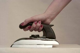 Eine Frauenhand mit rotlackierten Fingernägeln hält ein Bügeleisen