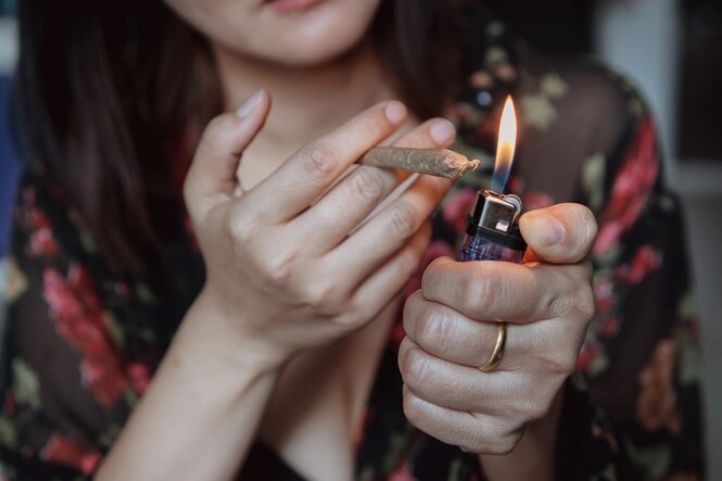 Eine Frau zündet einen Joint in ihren Händen mit einem Feuerzeug an