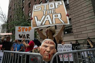 eine Frau hinter einem Absperrgitter hält ein Pappschild mit der Aufschrift 