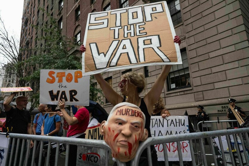 eine Frau hinter einem Absperrgitter hält ein Pappschild mit der Aufschrift "Stop the war" hoch.