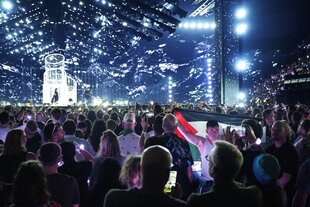 Ein Mann, der im Publikum steht während die israelische ESC-Teilnehmerin Yuval Raphael auf der Bühne performt, hält eine Palästina-Fahne in die Höhe