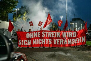 Menschen halten ein rotes Transparent, darauf steht geschrieben: "Ohne Streik wird sich nichts verändern"