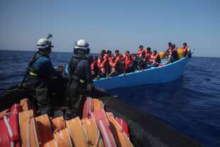 Ein Boot von Helfer:innen nähert sich auf dem Mittelmeer einem anderen Boot mit Geflüchteten, die Rettungswesten tragen