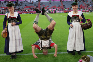 Eine Trachtengruppe auf dem Rasen der Arena in München. Einer macht dabei einen Kopfstand.