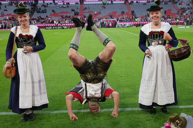 Eine Trachtengruppe auf dem Rasen der Arena in München. Einer macht dabei einen Kopfstand.