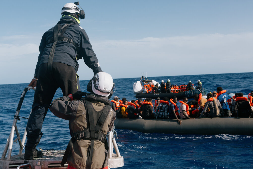 Ein überfülltes Schlauchboot auf dem offenen Meer, Retter nähern sich