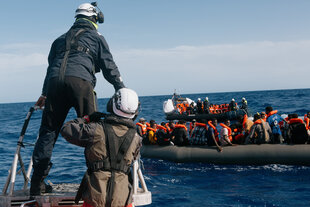Ein überfülltes Schlauchboot auf dem offenen Meer, Retter nähern sich