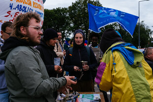 Drei Aktivist:innen in Regenkleidung protestieren vor dem Flüchtlingslager in Tegel