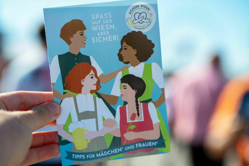 Eine Person hält einen Flyer vom Oktoberfest mit Hinweisen zu einem Safe-Space für Mädchen und Frauen auf dem Festgelände
