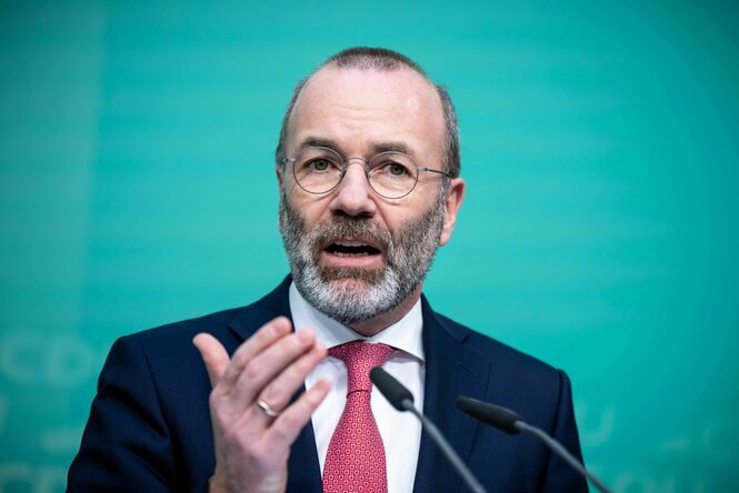 Manfred Weber spricht und gestikuliert vor einem türkisen Hintergrund