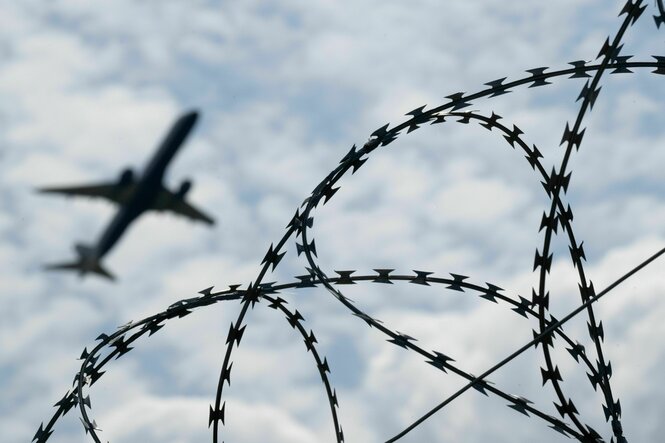 Ein Flugzeug hebt am Flughafen BER hinter einem Zaun mit Natodraht ab