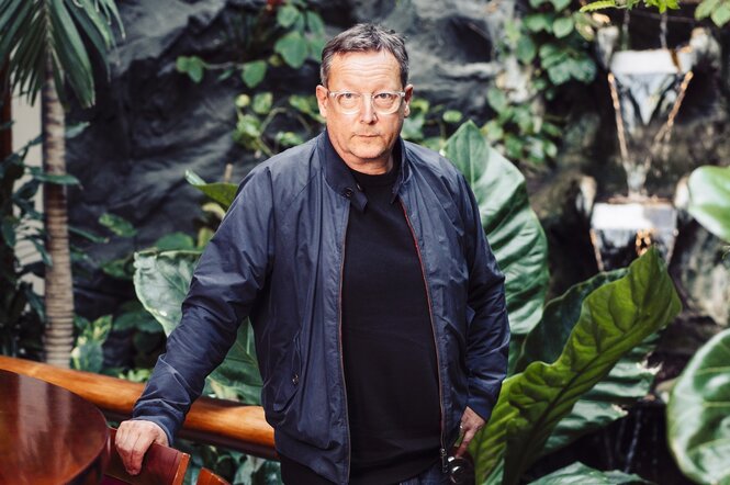 Zu sehen ist der Schauspieler Matthias Brandt. Im Hintergrund befindest sich viel Botanik.