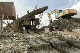 Bagger und Förderanlage bei einer Kies- oder Gesteinswaschanlage mit abfließendem Wasser und Geröll.